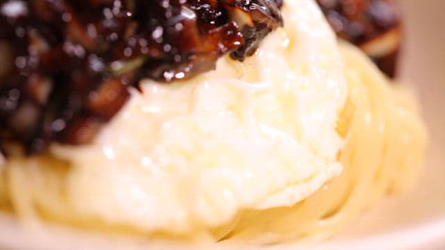 Bowl of noodles in thick black bean sauce with a fried egg