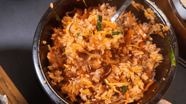 Spoon scooping up spicy oven-baked pork trotters mixed with vegetables.