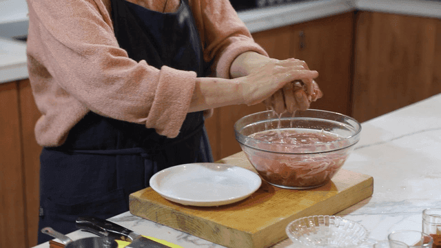 Woman squeezing moisture out of thinly sliced ​​duck meat in kitchen