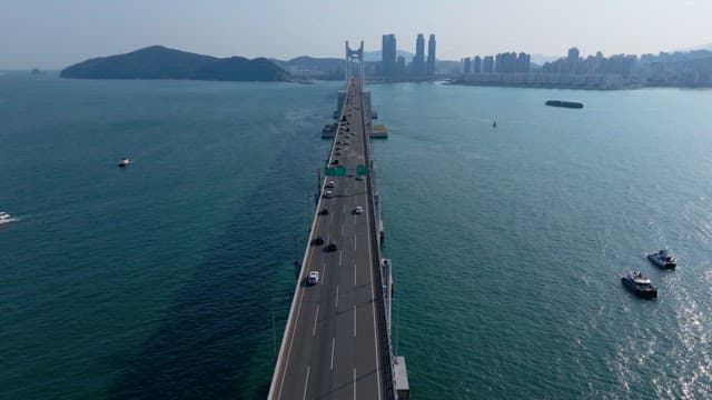 Cars driving over a Gwangan Bridge across the sea towards a city