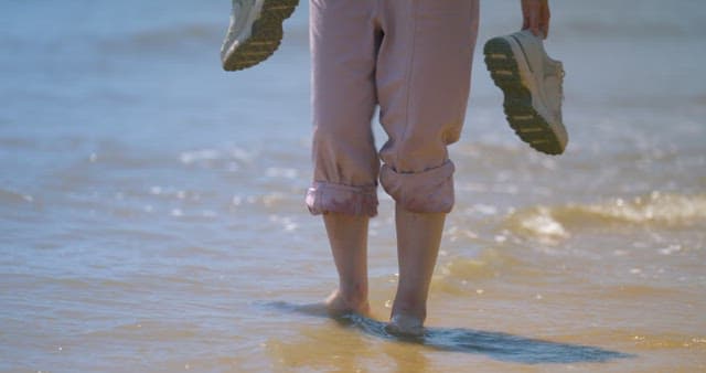 Person Walking on the Sandy Beach with Pants Rolled Up