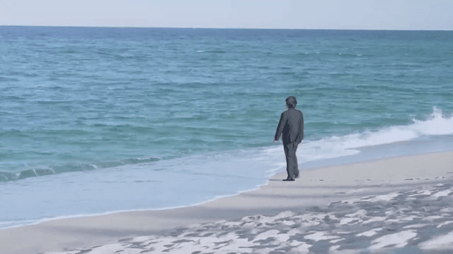 정장을 입은 남자가 해변을 걷고 있는 모습