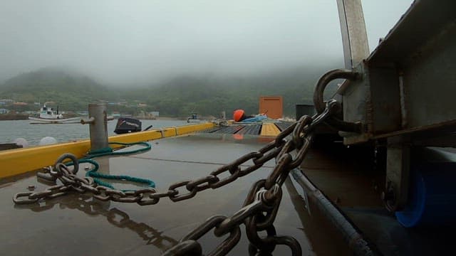 A foggy morning on a boat with chains and ropes on deck