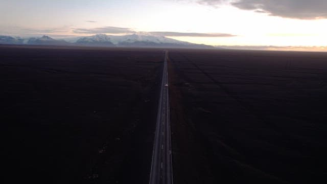 Car driving on a long road under a sunset sky