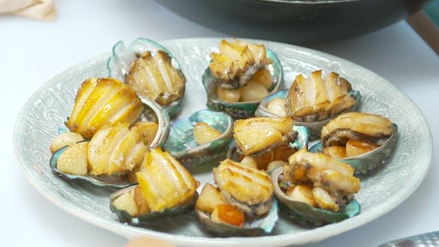 Appetizing butter-grilled abalone plated on a plate with tongs