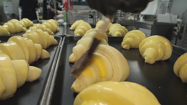 Croissants being brushed with egg wash in a bakery kitchen