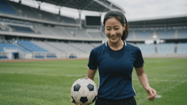 Female soccer player holding soccer ball on field