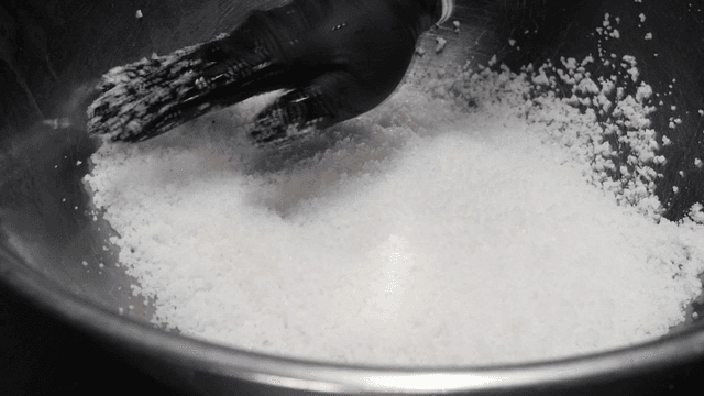 Salt poured into metal bowl with gloved hands