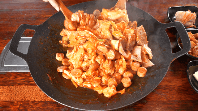 Spatula mixing stir-fried sausage in hot pan