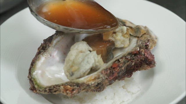 Sauce being poured over a cooked oyster