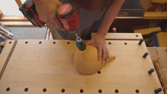 Person drilling a gourd on a workbench