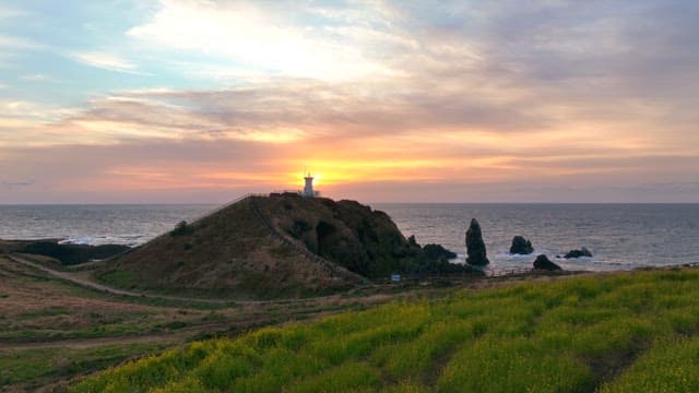 Lighthouse on a hill at sunset by the sea