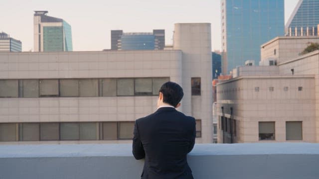 Man in a suit looking at buildings from a rooftop