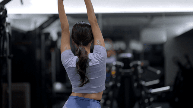 Back view of young woman stretching arms at gym