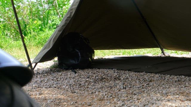 Setting up camping equipment under a tent near greenery