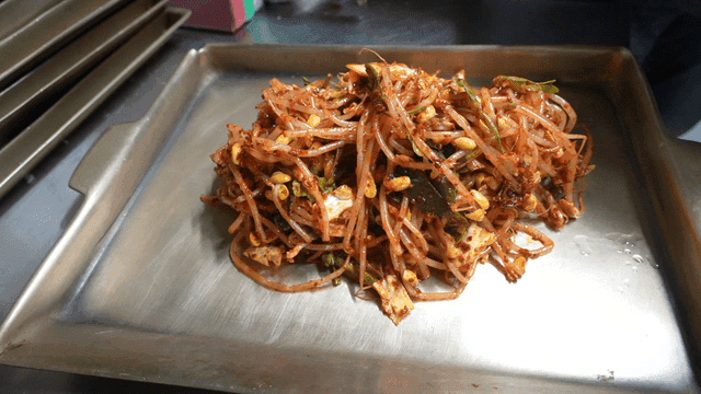 Hand placing spicy seasoned bean sprouts on tray