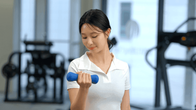 헬스장에서 정면을 보고 덤벨로 운동하는 여성