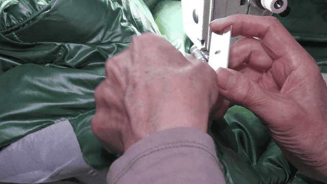 밝은 조명 아래 녹색 패딩을 바느질하는 모습