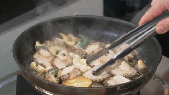 Fresh abalone being cooked with garlic in a pan.