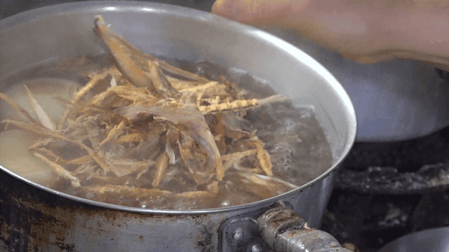 Pot simmering with corn and onions on a stove adding dried pollock strips