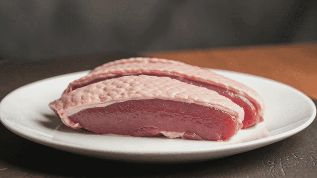 Raw duck breast on a white plate