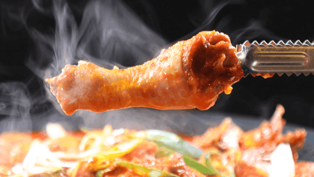 Tongs holding chicken leg in spicy chicken stew with vegetables