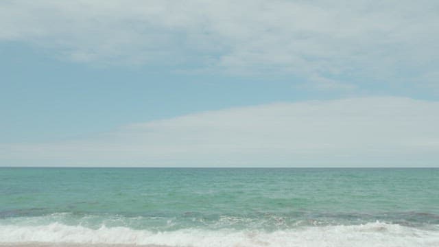 해변가에서 잔잔히 물결치는 파도와 연한 빛깔의 하늘