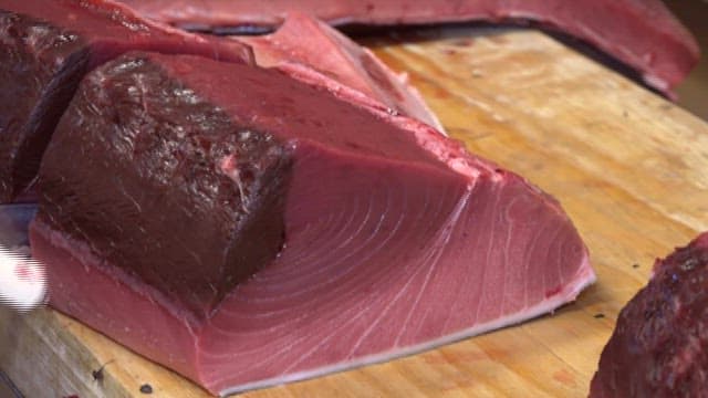 Fresh tuna being cut with a knife on a cutting board