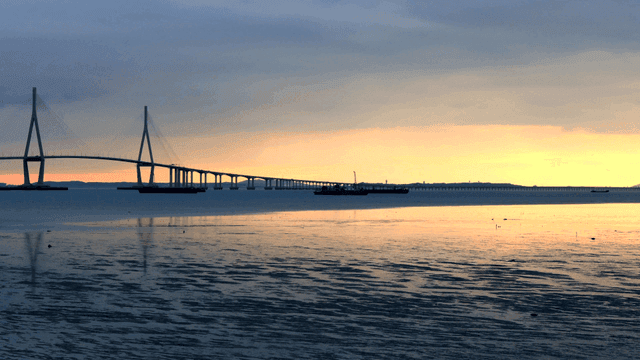 Bridge over calm mudflat sea at sunset