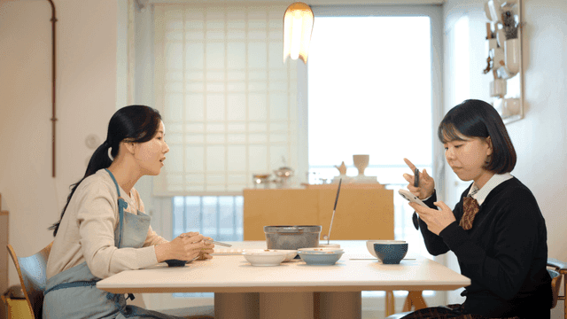 Mother nags her daughter for using her smartphone at dinner table.