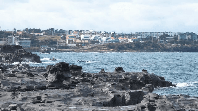 파도가 치는 바위 해안과 멀리 보이는 마을