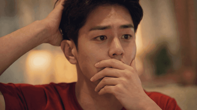 Man in red T-shirt covering his mouth with his hand, lost in thought