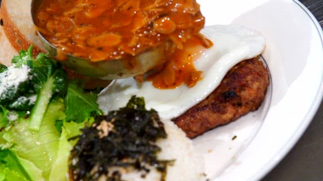 Sauce being poured over hamburger steak with a fried egg