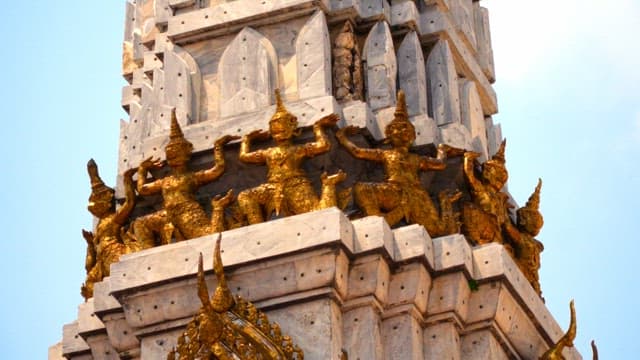 Elaborate golden Buddha statues on the outer wall of a pagoda in a Thai temple