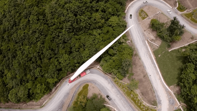 울창한 산 속 구불구불한 도로에서 풍력 터빈 자재를 운반하는 모습