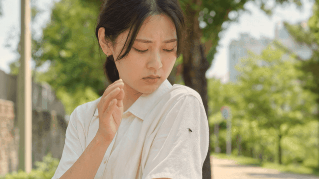 Woman who swatts away fly sitting on her shoulder with her hand