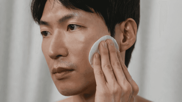 Man applying skincare with a cotton pad