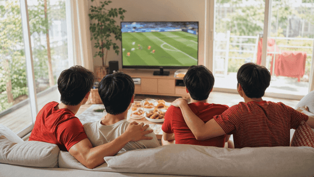 Backs of friends cheering while watching soccer match at home