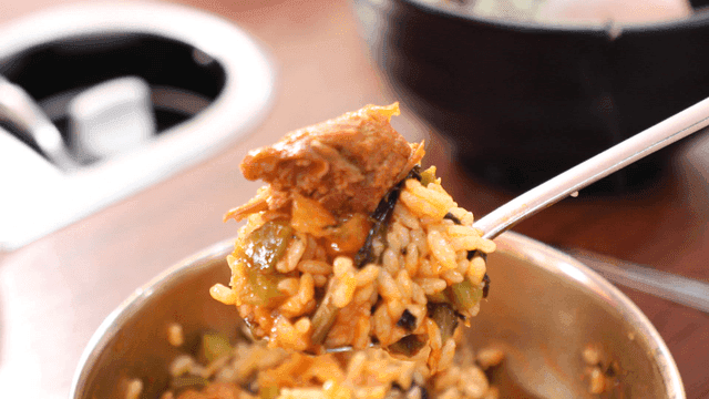 Spoonful of rice mixed with sauce and topped with meat