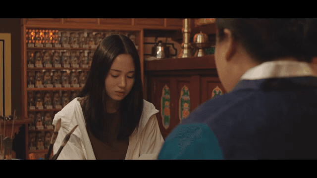 Shaman and a woman conversing in a fortune teller's shop