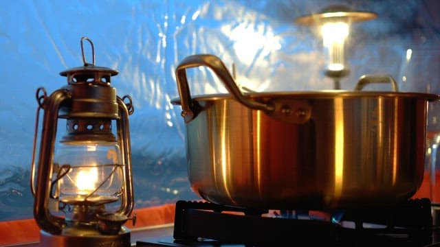 Illuminated camping lantern next to the pot with food