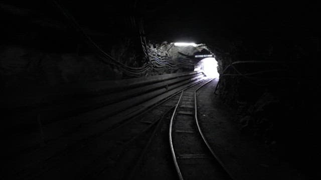 Railroad track leading from a dark coal mine to the bright outside