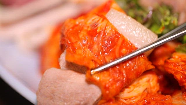 Kimchi and boiled pork slice held with chopsticks