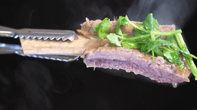Tongs lifting hot galbitang topped with vegetables