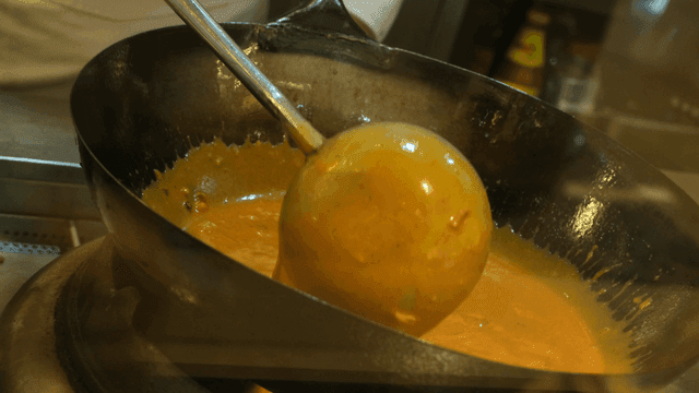 Ladle stirring curry sauce in hot wok