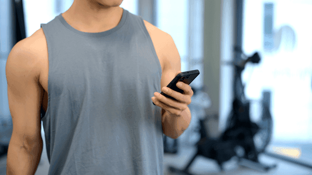 헬스장에서 작은 덤벨을 들며 스마트폰을 사용하는 남성