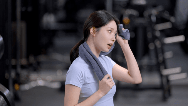 헬스장에서 운동 후 수건으로 땀을 닦고 정면을 보고 미소짓는 젊은 여성