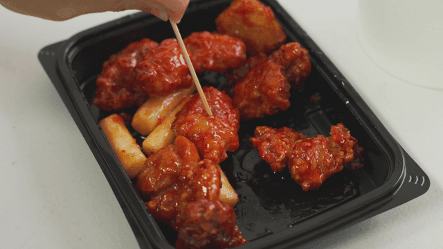 Spicy chicken gangjeong with rice cakes on a plastic plate