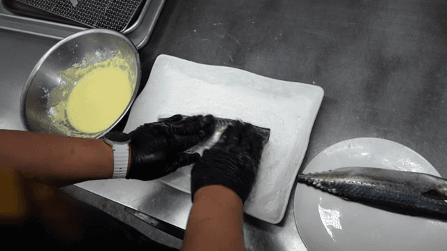 Fish being coated with flour in a kitchen
