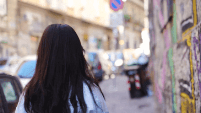 Back view of long-haired woman walking along graffiti wall